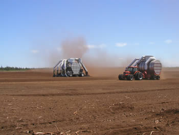 Large vacuums being driven over the Grande-Anse Peat Bog to collect the loosened peat moss.